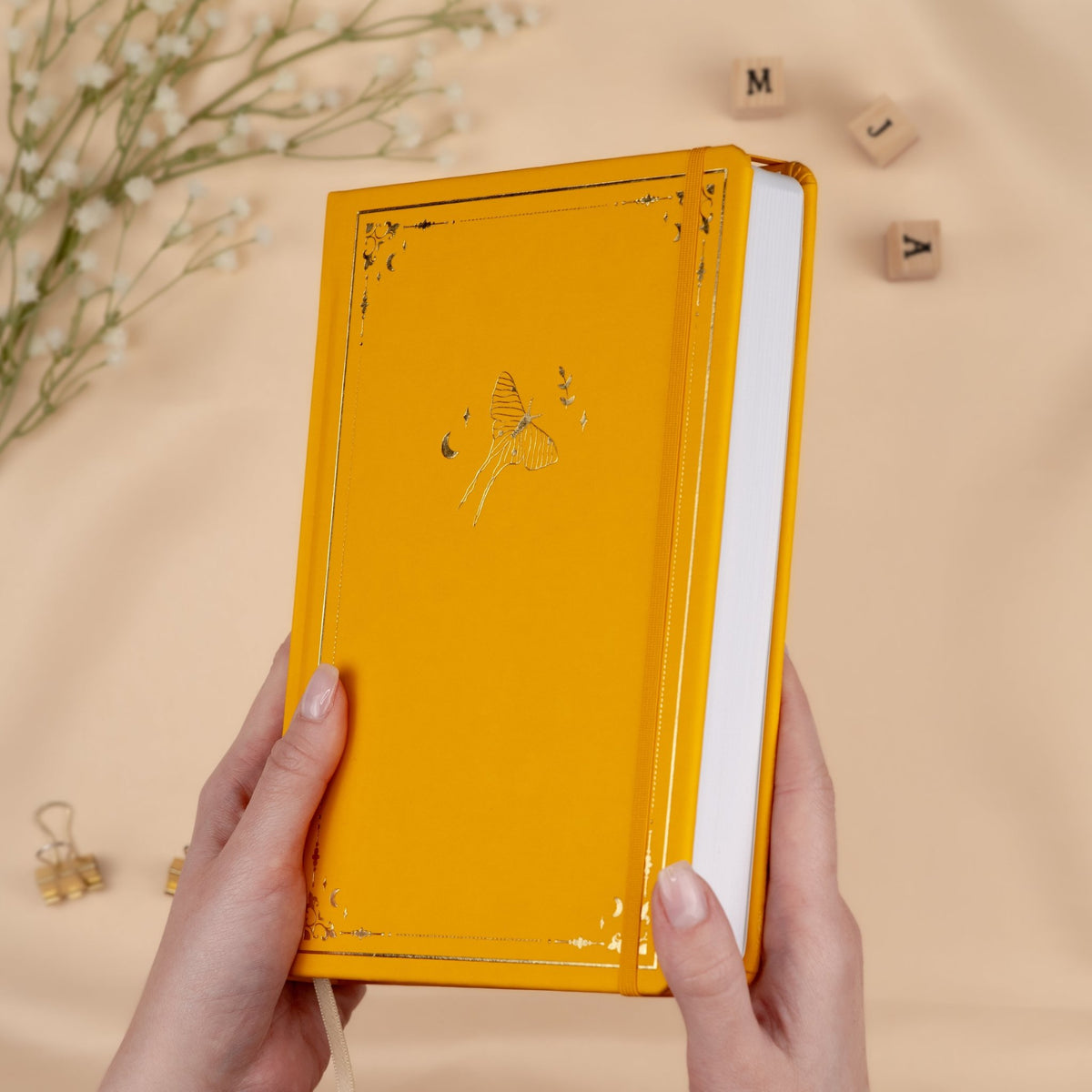 Holding a yellow Honey Spice premade dotted bullet style journal made of Italian vegan leather with an embossed gold luna moth design.