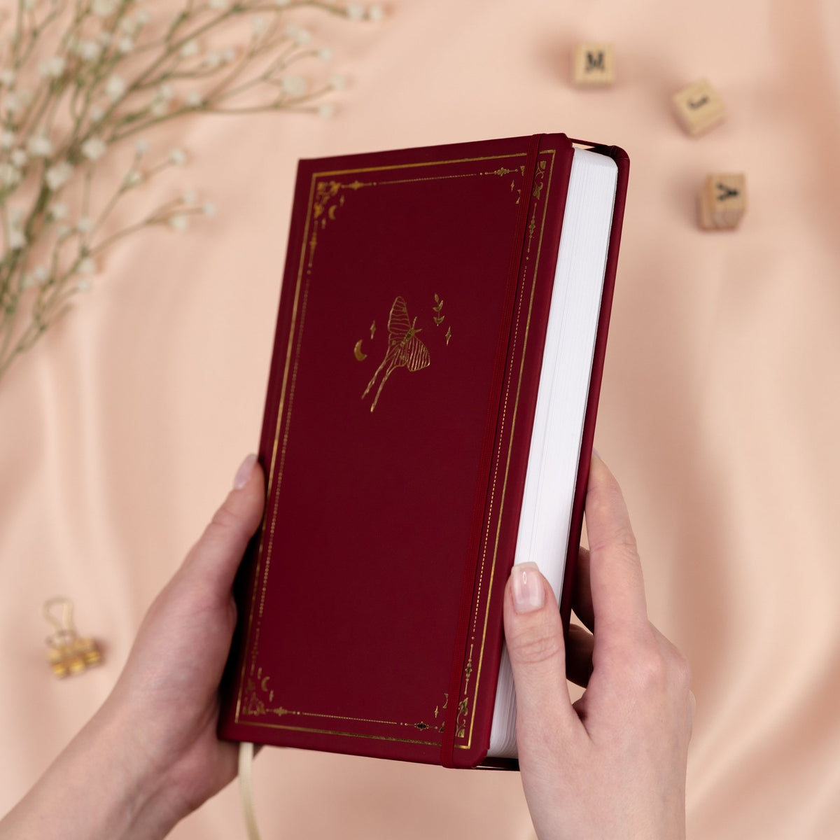 Holding a Forbidden Fruit red premade dotted bullet style journal made of Italian vegan leather with an embossed gold luna moth design.
