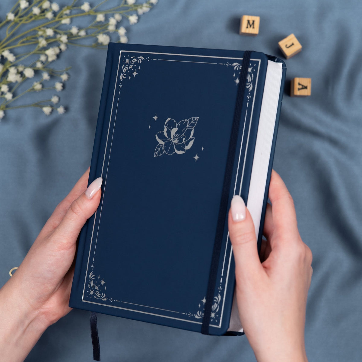 Holding a blue Midnight premade dotted bullet style journal made of Italian vegan leather with an embossed silver magnolia design.