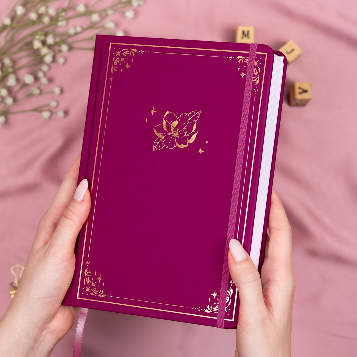 Holding a plum premade dotted bullet style journal made of Italian vegan leather with an embossed gold magnolia design.