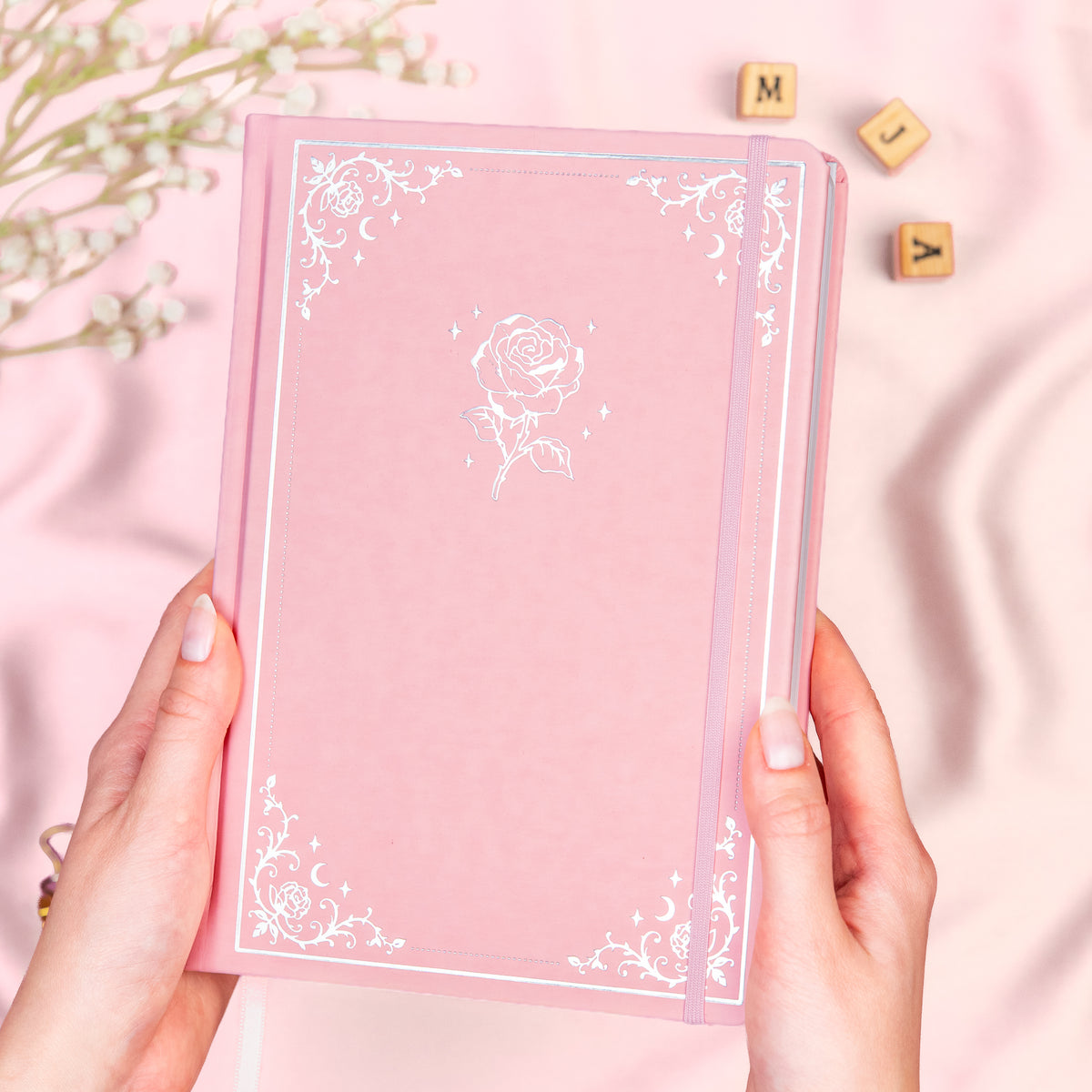 Holding a pink pre-designed dotted bullet style journal made of Italian vegan leather with an embossed gold rose design.