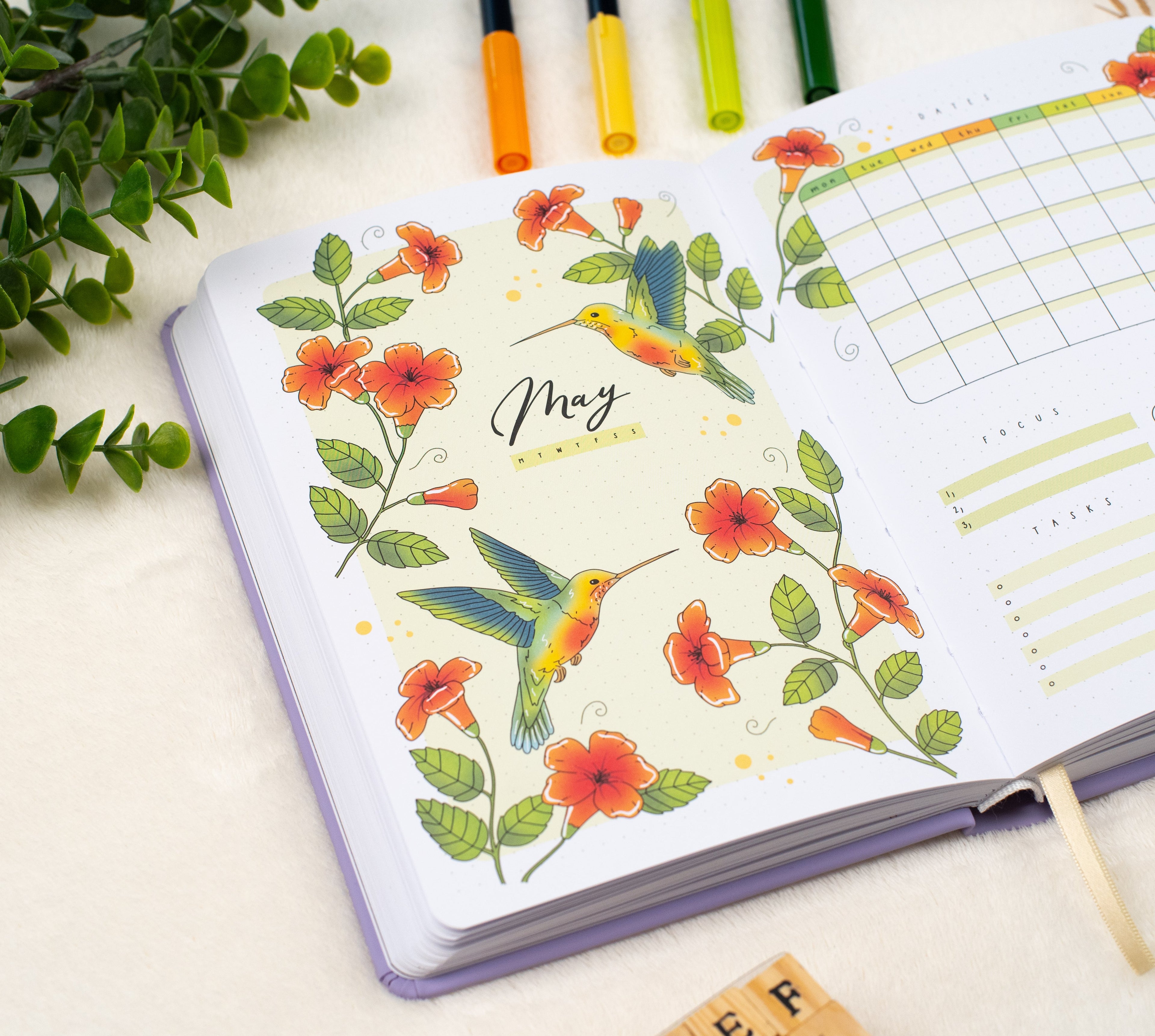 Opened hand drawn premade bullet style journal on a May cover page with hummingbirds and trumpet flowers.