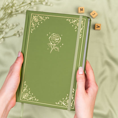 Holding a mossy green premade dotted bullet style journal made of Italian vegan leather with an embossed gold rose design.